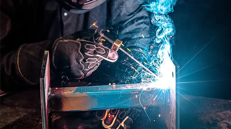 Welder in protective gear stick welding a metal piece, with sparks and smoke visible