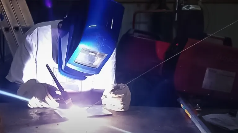 Person welding with a TIG welder, wearing a protective helmet and gloves