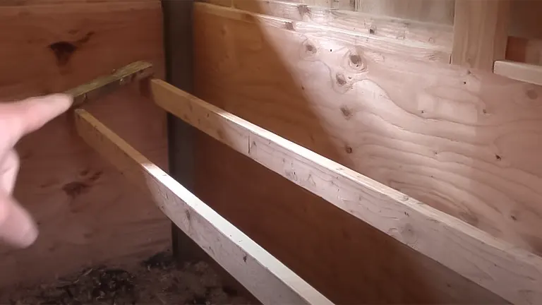 Hand pointing to wooden roosting bars inside a chicken coop