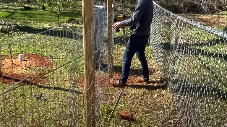 Individual working on a chicken run, attaching wire mesh to wooden posts