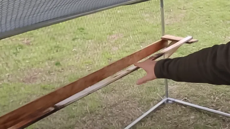 Hand installing a wooden perch in a chicken coop with wire mesh