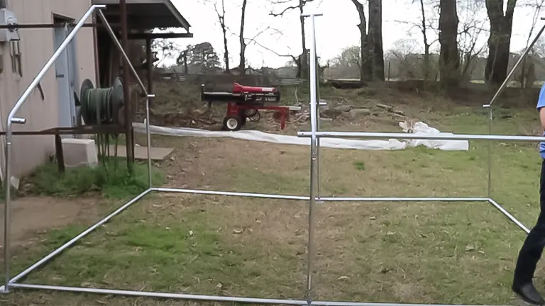 Partial frame of a chicken coop on grass with background farm equipment