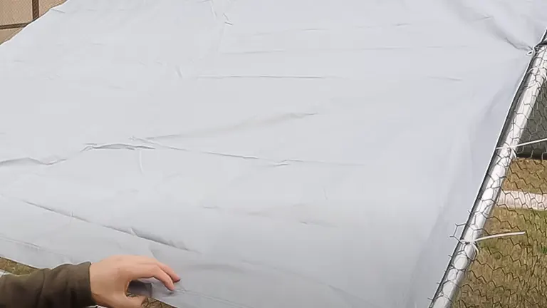 Hand securing a tarp over a chicken coop frame with chicken wire visible