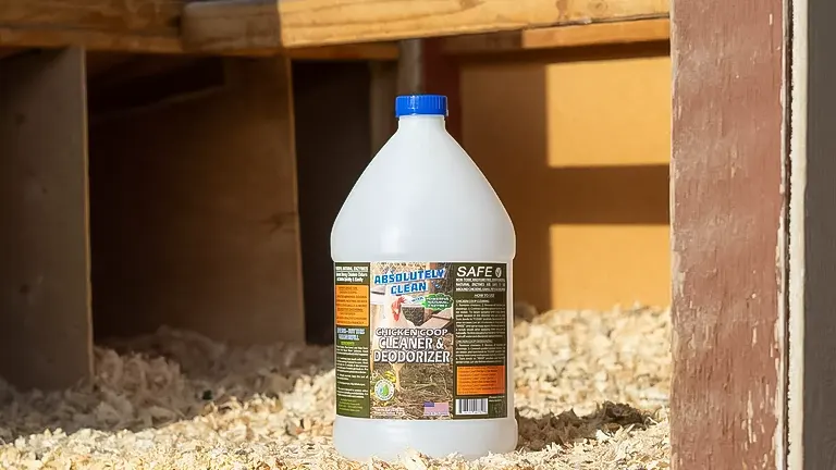 Bottle of coop cleaner and deodorizer placed inside a wooden chicken coop with bedding visible