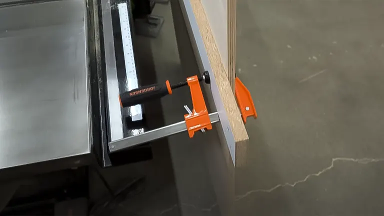 Clamp and metal guide attached to plywood on a table saw