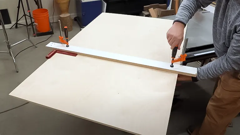 Person clamping a straight edge to plywood for cutting