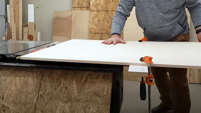 Person preparing to cut plywood on table saw with straight edge guide
