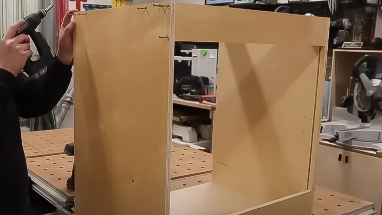 Person using a drill on the side of an unassembled wooden frameless cabinet