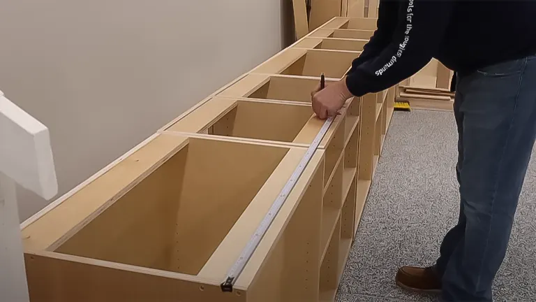 Person measuring the alignment of frameless cabinets with a level