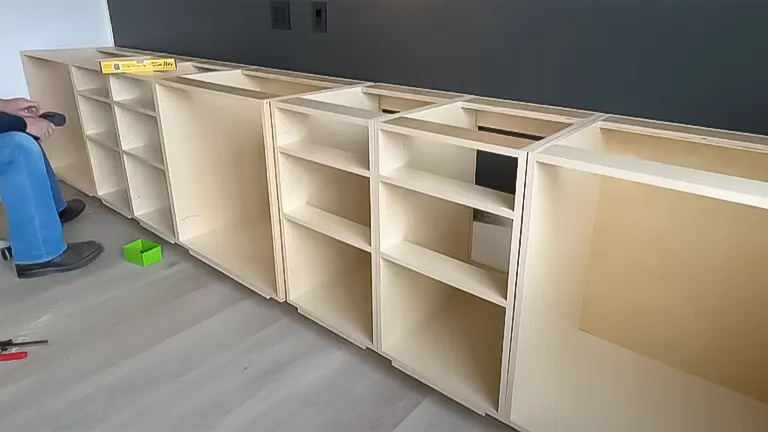 Person installing and leveling a series of frameless wooden cabinets