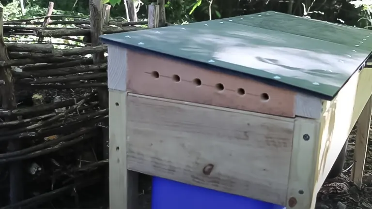 A wooden compost bin with a metal lid and ventilation holes, part of a DIY setup for soldier fly larvae composting
