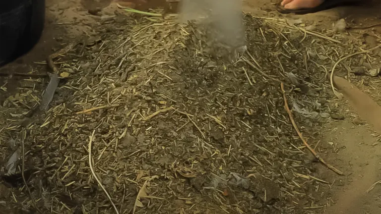 Steaming pile of compost material with a shovel and bare feet visible