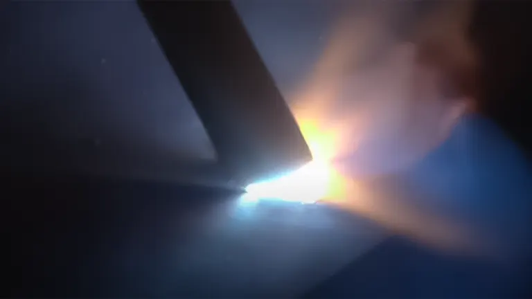 Bright arc and sparks visible as a welder runs a bead in stick welding