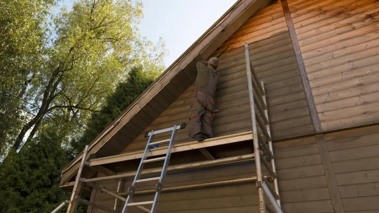 Man with ladder installing siding of barn