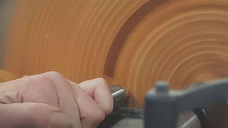 Close-up of hands using a tool on a spinning piece on a wood lathe