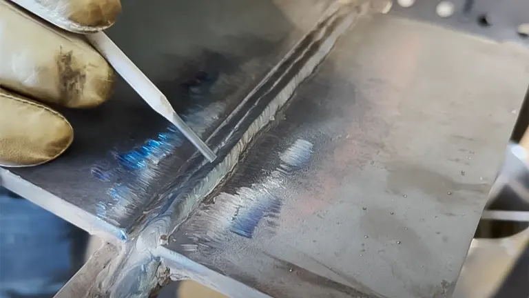 Close-up of a welded joint on metal plates with a gloved hand holding a 7018 electrode