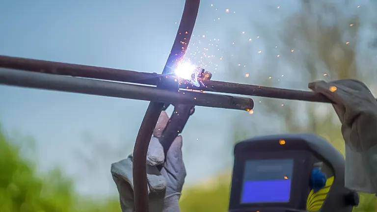 Welder in protective gear performing stick welding on metal rods outdoors