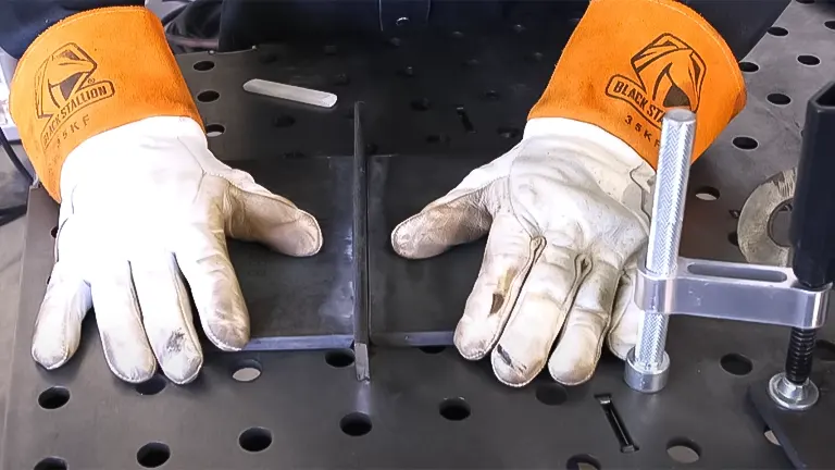 Hands in protective gloves positioning metal plates for welding on a perforated work table
