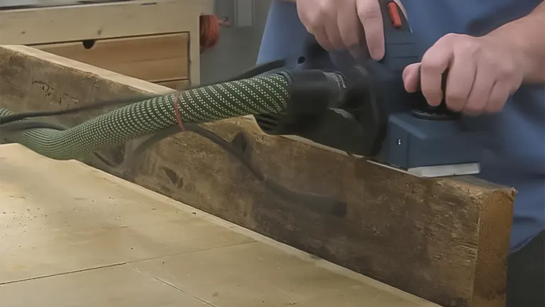 Woodworker planing timber with an electric hand plane and dust hose