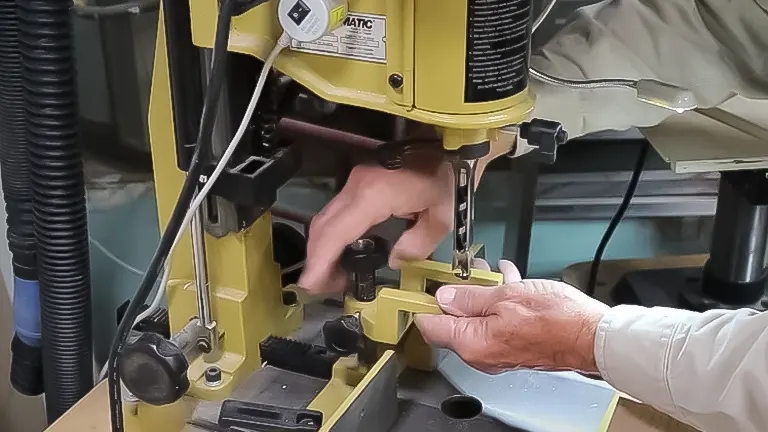 A person's hands adjusting the hold-down mechanism on a Powermatic PM701 Benchtop Mortising Machine.