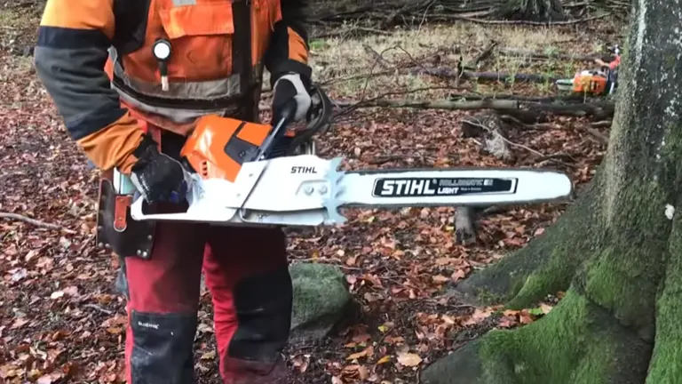 Forestry worker in safety gear preparing to use a STIHL chainsaw in a forest setting.