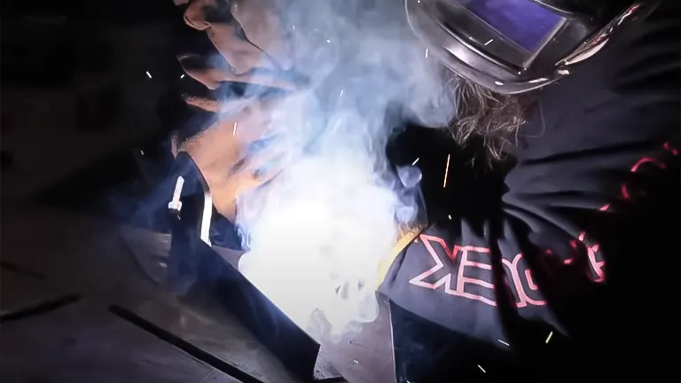 Welder at work wearing a mask, with bright welding arc and smoke