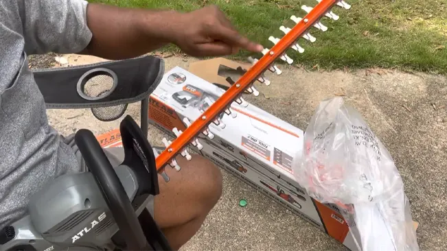 Person assembling an orange and white hedge trimmer outdoors