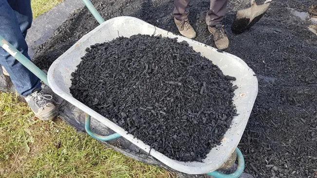 Wheelbarrow filled with black mulch, person standing nearby