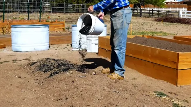 Person pouring soil into a garden bed