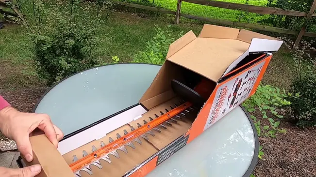 person unboxing a new hedge trimmer outdoors on a glass table