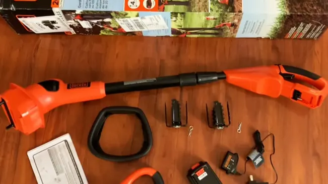 Disassembled orange and black leaf blower with accessories and manual on a wooden floor