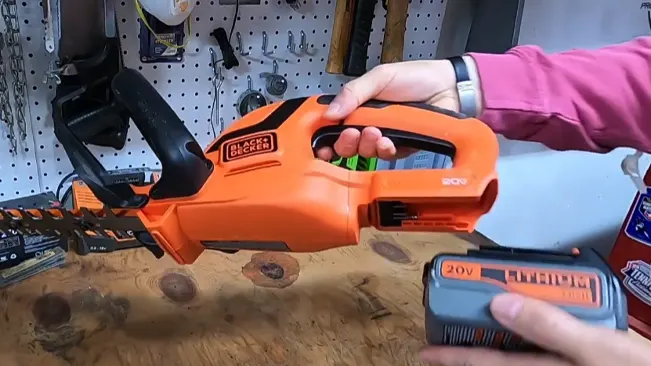 person inserting a 20V BLACK+DECKER battery into an orange chainsaw
