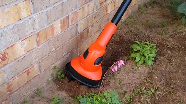 An orange and black trimmer edging grass against a brick wall