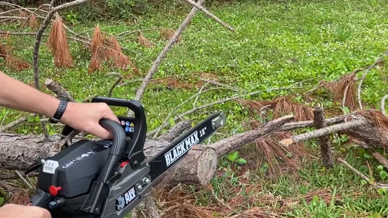 Person using a BLACKHAWK 18 chainsaw to cut through fallen tree branches on a grassy area.