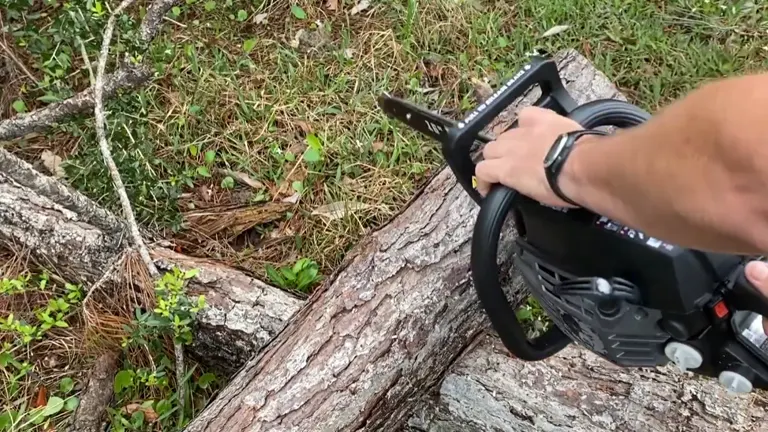 Person using a chainsaw to cut through a fallen tree trunk in an outdoor setting.