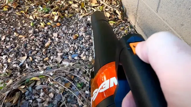 Person holding a leaf blower, preparing to clean a garden area with fallen leaves and debris.