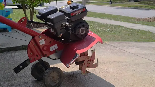 red tiller with a black engine, positioned on a concrete surface outdoors