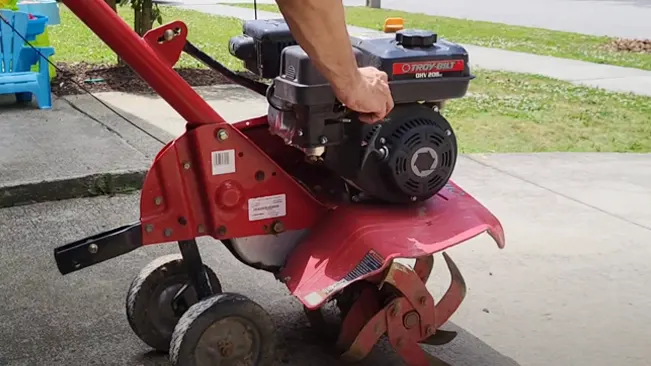 Person operating a red Troy-Bilt tiller with a black engine in an outdoor setting.