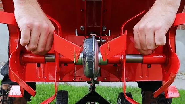 Person adjusting the blade of a red lawnmower on grass