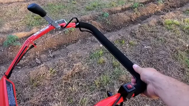 hand holding the handlebar of a red tiller, ready to ride on a grassy field