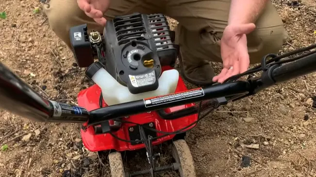 Person inspecting a red mini tiller outdoors