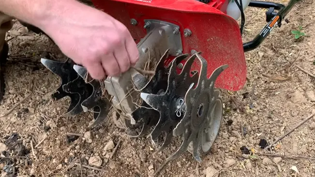 Person cleaning the blades of a red soil tiller