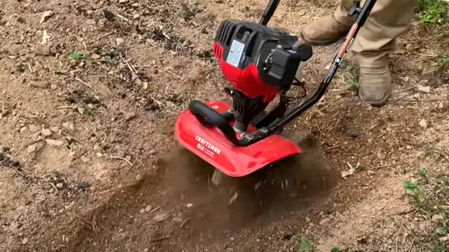 Person operating a red CRAFTSMAN tiller on dry, rocky soil