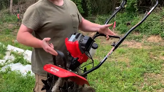 Person holding a red and black tiller in a garden