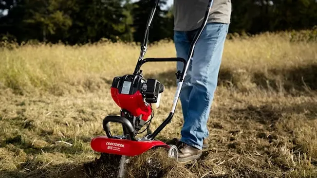 Person operating a red CRAFTSMAN tiller in a field