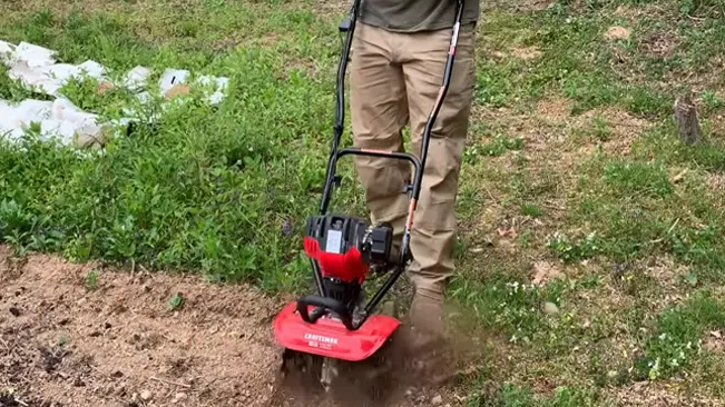 Person operating a red rototiller on grassy land