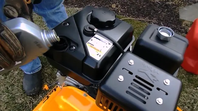 a person, visible from the waist down, refilling an orange and black portable generator with fuel from a silver metal container