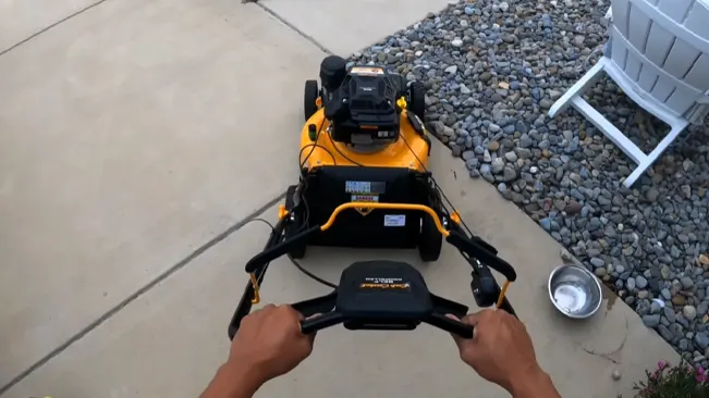 First-person view of operating a Cub Cadet lawnmower on a concrete path next to a gravel area