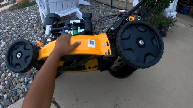 A person’s hand touching an overturned Cub cadet lawnmower on a gravel surface