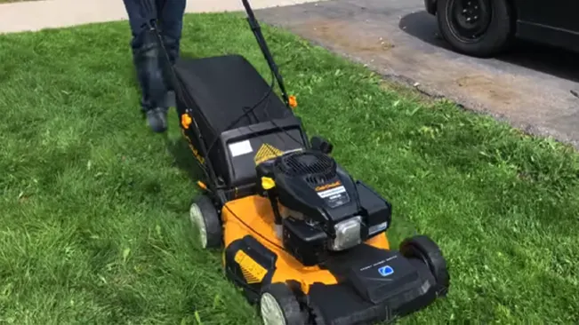 Person in dark clothing mowing a grassy area with a Cub Cadet